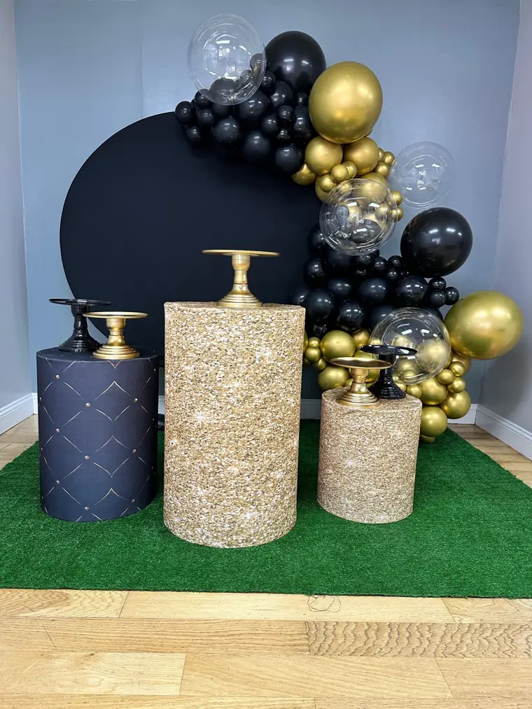 Decoração montada pela Party Decoration Fest no tema Preto e dourado: painel, arco de balões e cilindros com bandejas