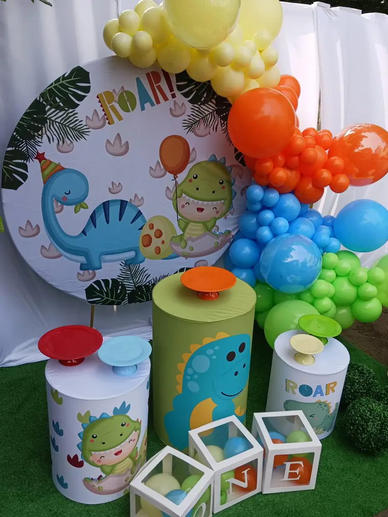 Decoração montada pela Party Decoration Fest no tema Dinossauro: painel, arco de balões e cilindros com bandejas