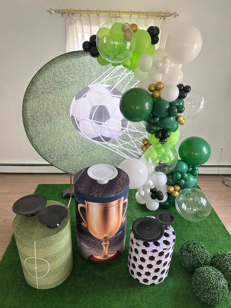 Decoração montada pela Party Decoration Fest no tema Campo de futebol: painel, arco de balões e cilindros com bandejas